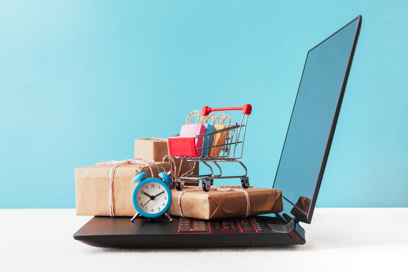 Internet shop / e-commerce sale and delivery service concept: shopping cart multicolored packages and boxes with trolleybus logo on laptop keyboard, blue background